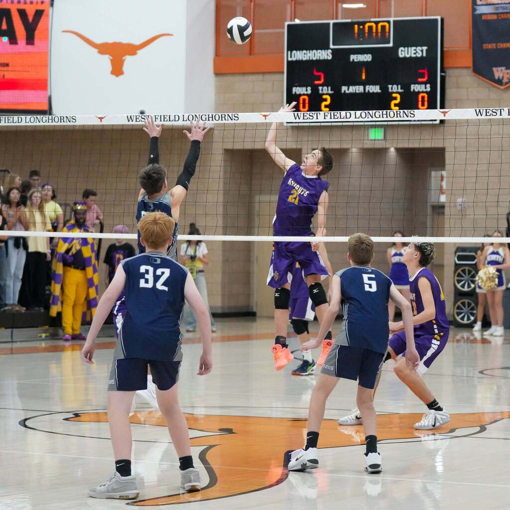 Image 2: A North Ogden Junior High player in a purple jersey leaping high at the net to spike the ball against opposing blockers.