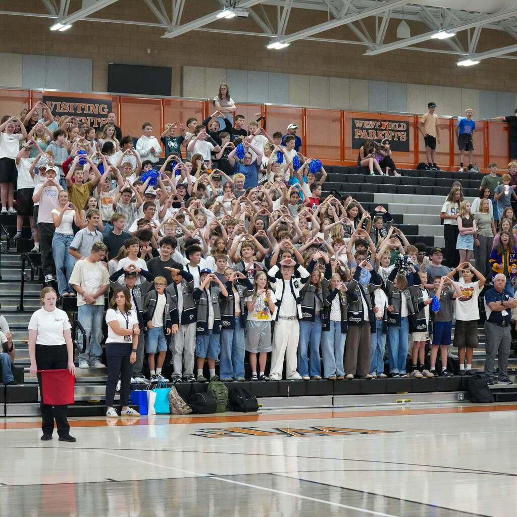 Image 9: A large crowd of students filling the gym bleachers, holding up heart hand signs to support their team during the game.