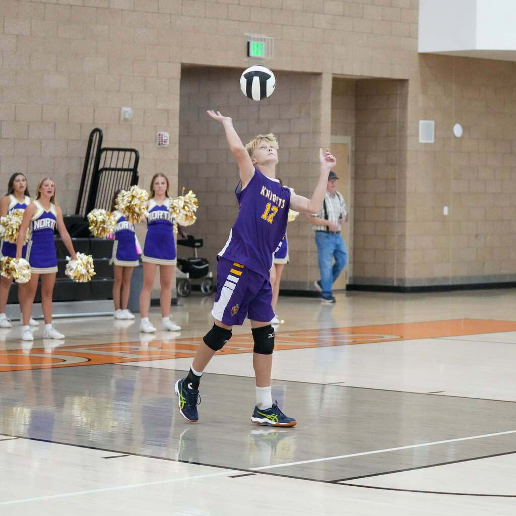 Image 4: A North Ogden Junior High player in a purple jersey setting the volleyball high near the net as cheerleaders watch from the sidelines.
