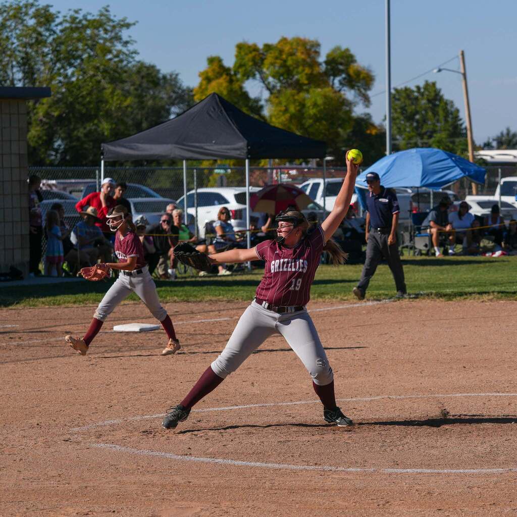 Image 8: A pitcher delivering a strike with power from the pitcher's mound while spectators watch from behind the fence.