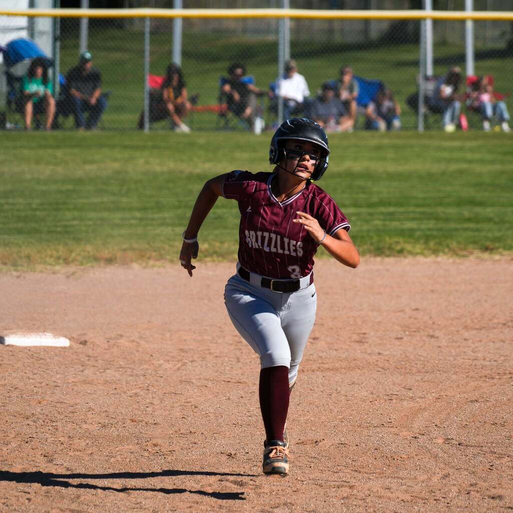 Image 6: A runner in a maroon uniform sprinting hard down the baseline toward the next base.