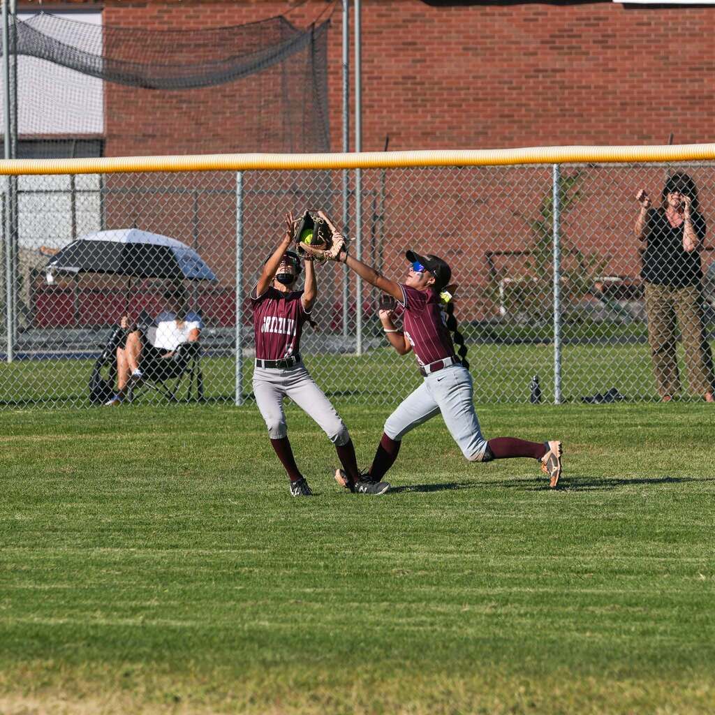 Image 3: Two outfielders tracking and leaping together to catch a pop fly ball in the grass outfield.