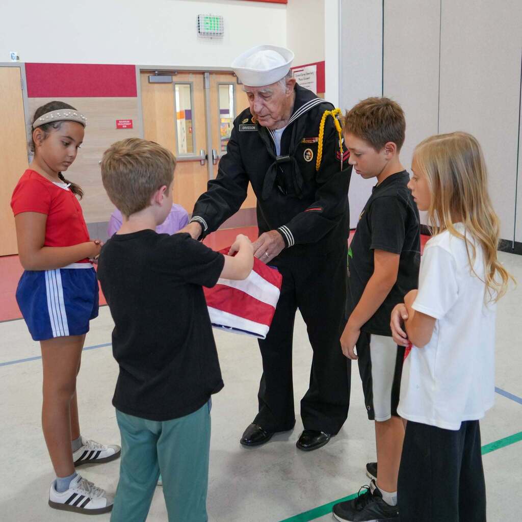 Image 8: A Navy veteran gathered with a small group of students demonstrating how to complete the final fold of the flag.