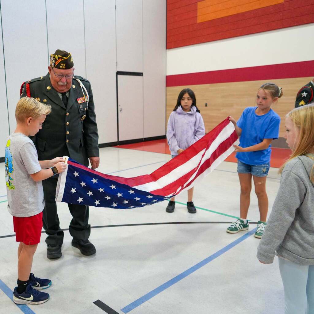 Image 6: An Army veteran inspecting and guiding students through the intermediate long fold of the American flag.