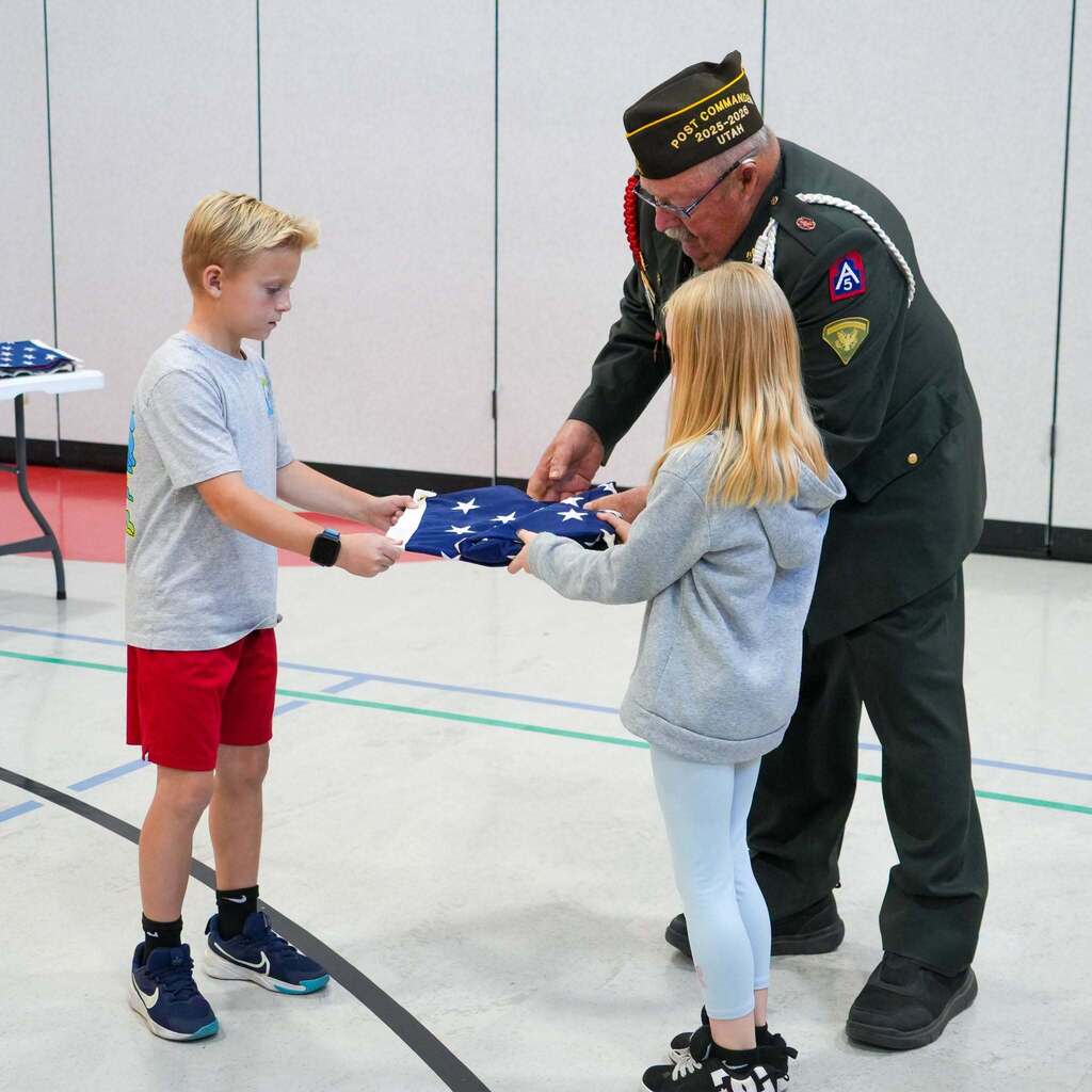 Image 9: An Army veteran helping two students place the proper final tuck into a neatly folded triangular flag.