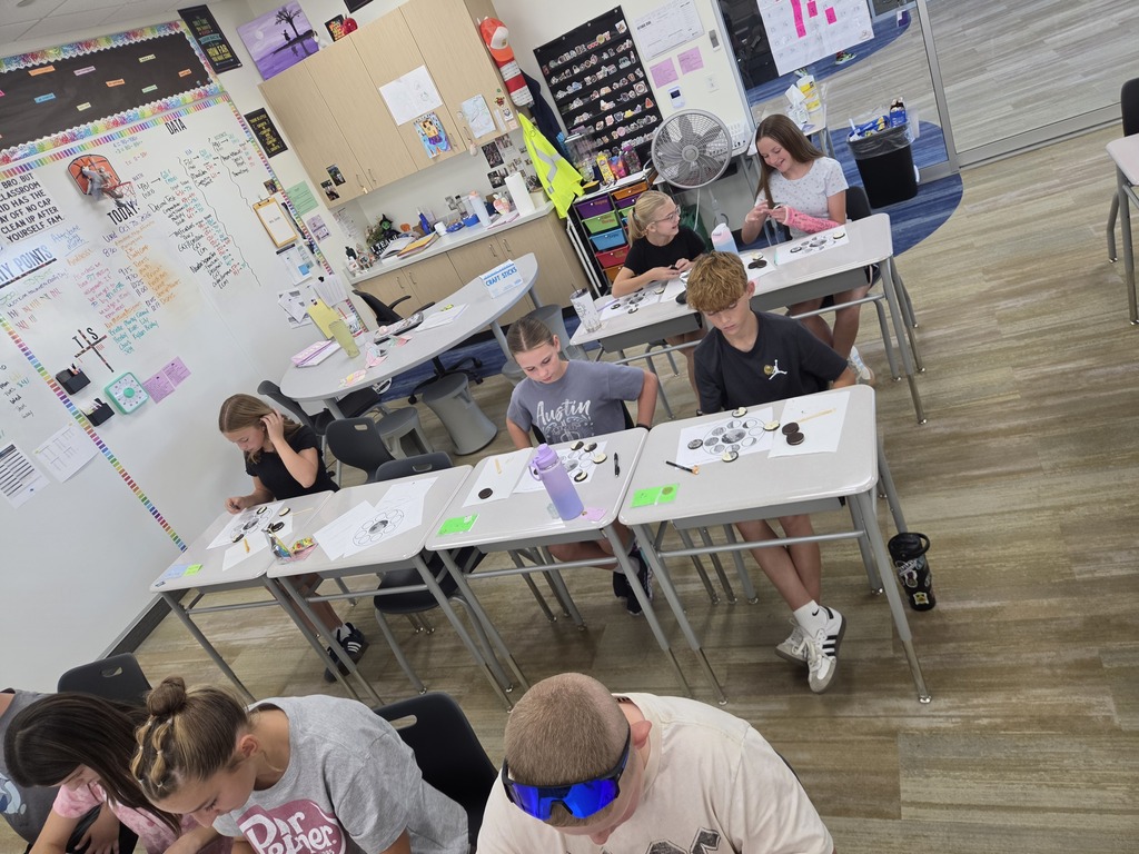 Classroom view showing several students working at desks with cookie moon phase worksheets, including students wearing "Austin" and "Dr Pepper" shirts.