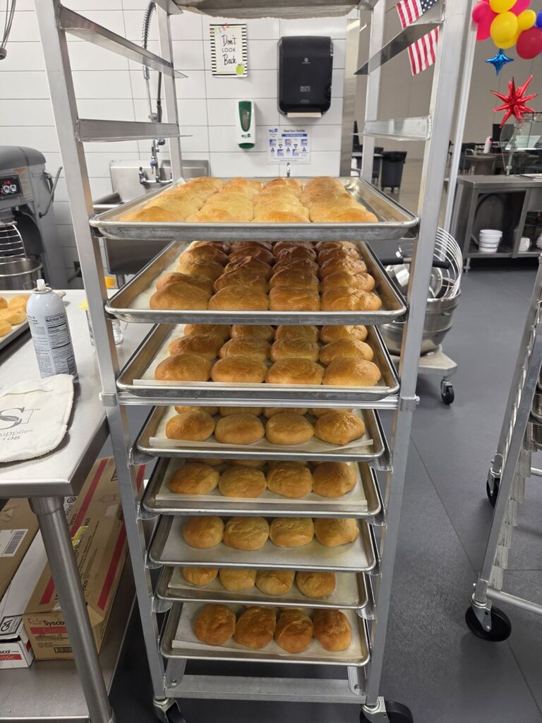 A tall metal bakery rack filled with sheet pans containing freshly baked rolls.