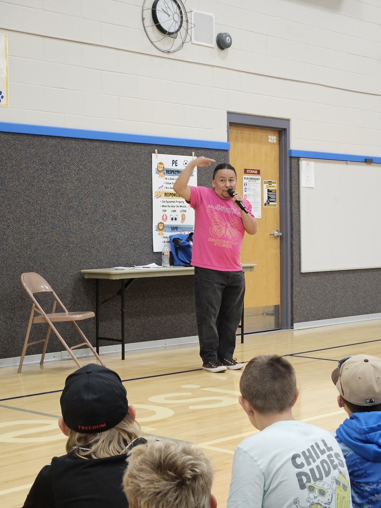 Nestor gesturing with his hand high above his head while sharing a story into the microphone during a school assembly.