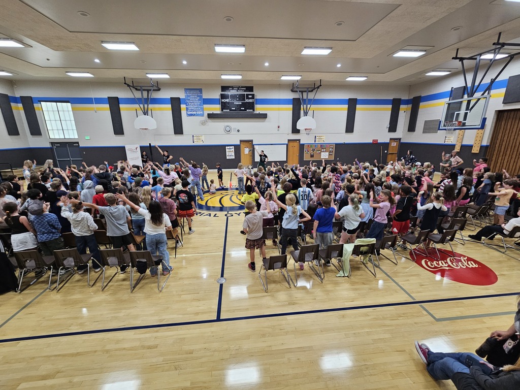 Wide view of the entire gym packed with students standing up and participating in the school dance assembly.