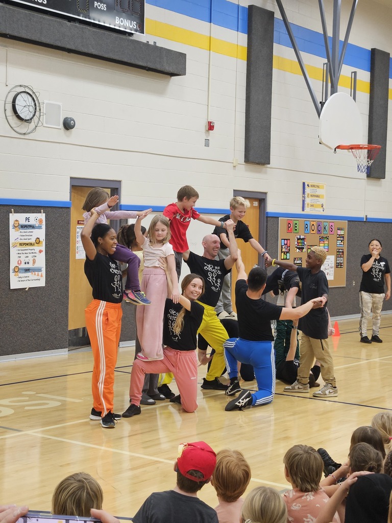 Dance troupe performing a high-energy pyramid stunt in a school gymnasium surrounded by cheering students.