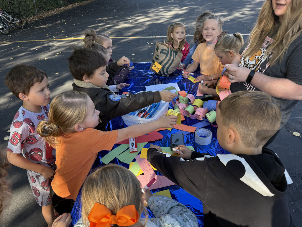Close-up overhead view of kindergarteners actively gluing and linking paper strips to construct a long paper chain together. 