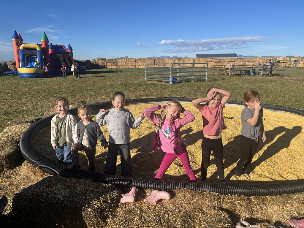  Six young girls posing and making fun faces inside a large outdoor corn pit filled with dried corn kernels.