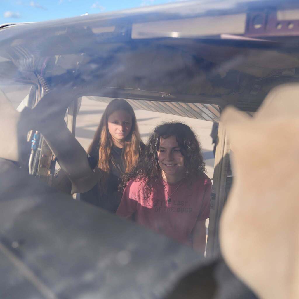 Image 9: A view looking inside the frame of an aircraft, showing two smiling female students looking through the window frame.