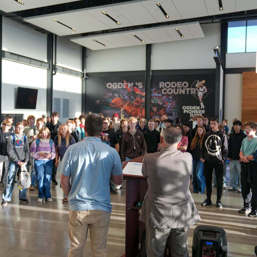 Image 4: An audience of students gathered inside a large event hall with "Ogden's Rodeo Country" graphics on the wall, listening to a speaker presenting at a podium.
