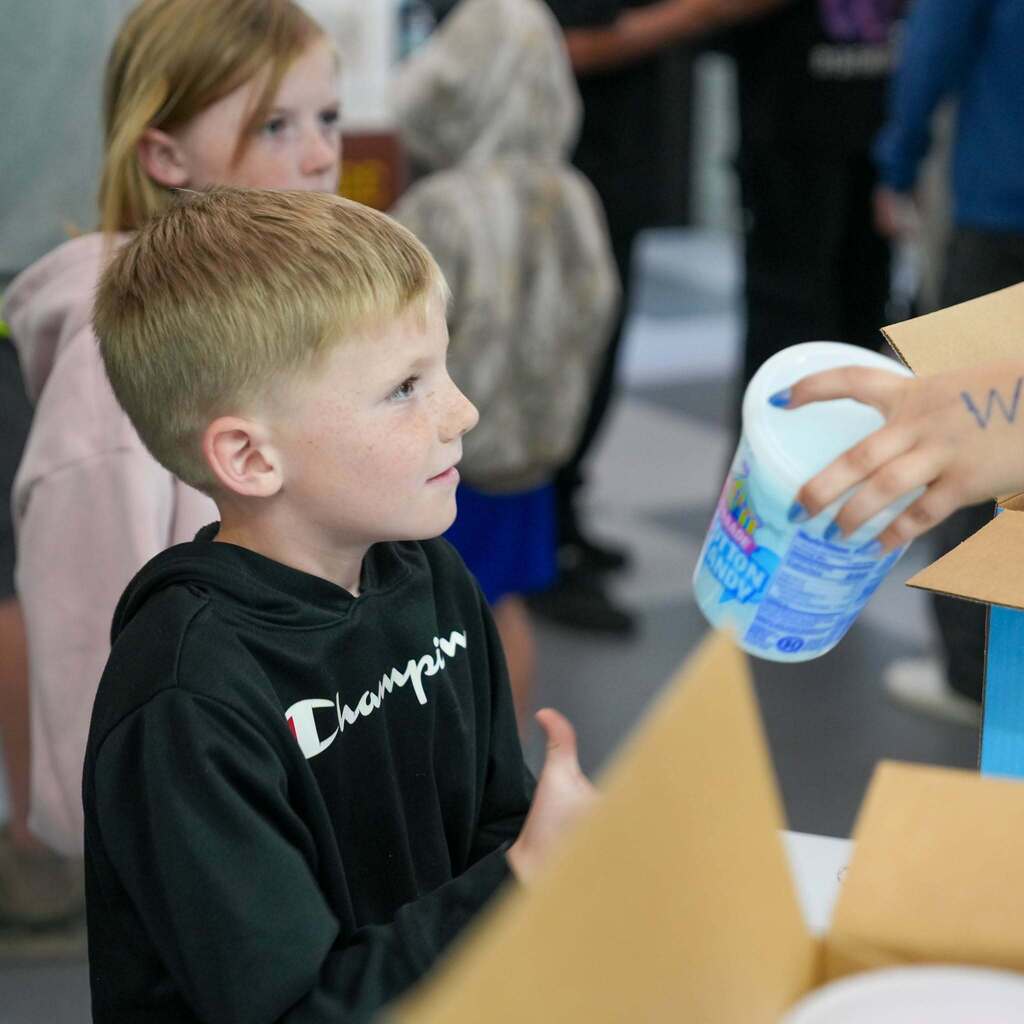 Image 2: Close-up of a young boy in a black Champion hoodie receiving a tub of cotton candy from a student volunteer during a school event.