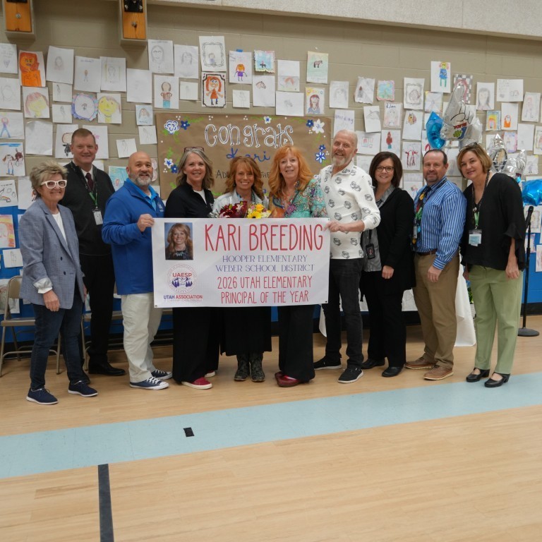 Weber School District leadership and staff standing together in the Hooper Elementary gym, holding a large banner that reads "Kari Breeding: 2026 Utah Elementary Principal of the Year."