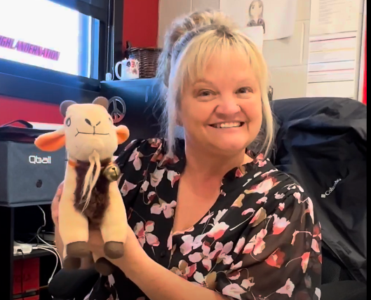 A woman in a flowered shirt holding a goat stuffed animal