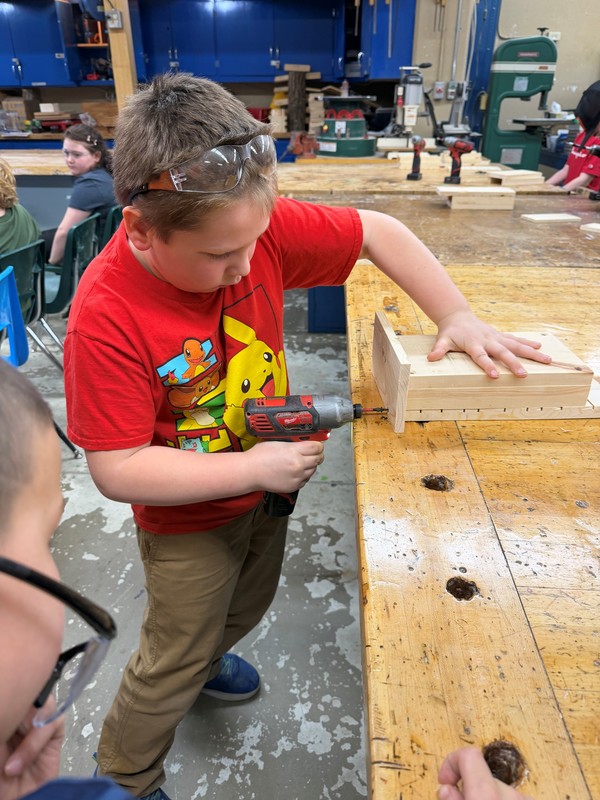 Student in red shirt assembling a bat house.