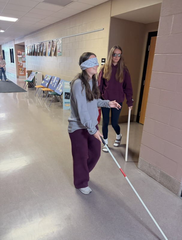 Disability Awareness training with two students blindfolded walking in the hallway.