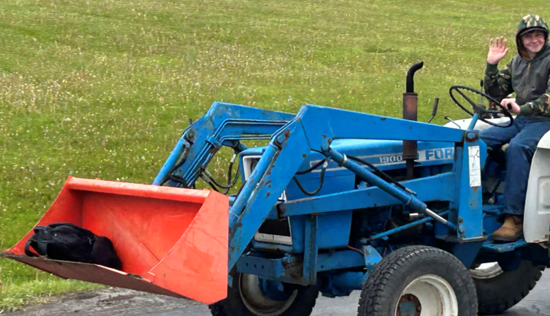 FFA student driving to school with backpack in the loader bucket.