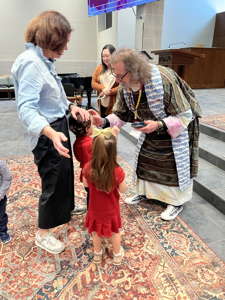 Mister Bruce puts ashes on two Pre K students' foreheads.