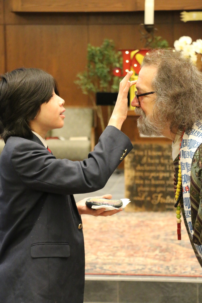 Mister Bruce has ashes placed on his forehead by a student.