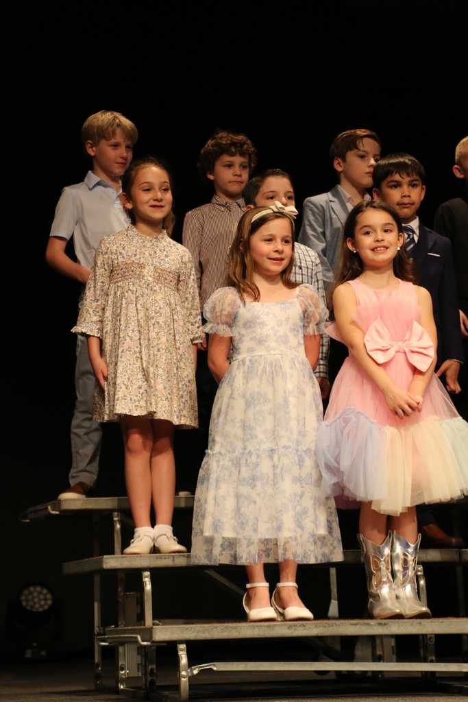 First grade students smile on stage.