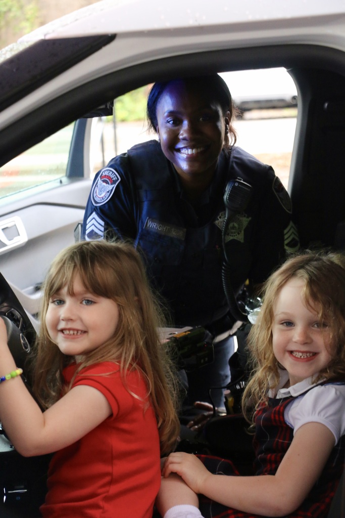 Students smile with an officer as they "drive" the police car.