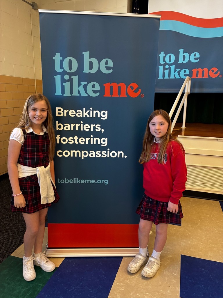 Two third grade girls smiling in front of the To Be Like Me banner.
