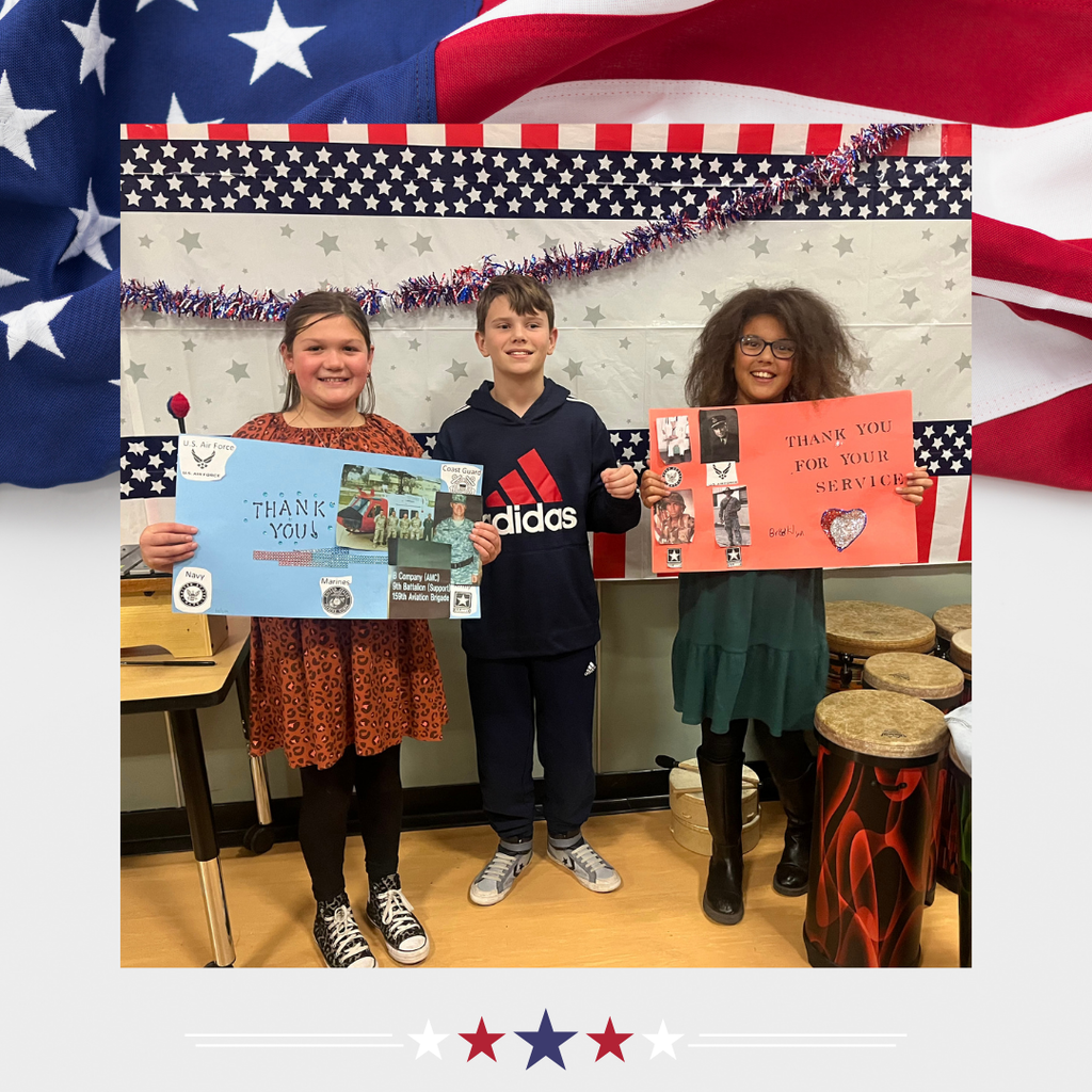 Picture: American Flag background. Picture of three students- two of whom are holding signs. The signs are blue and red and thank Veterans for their service.