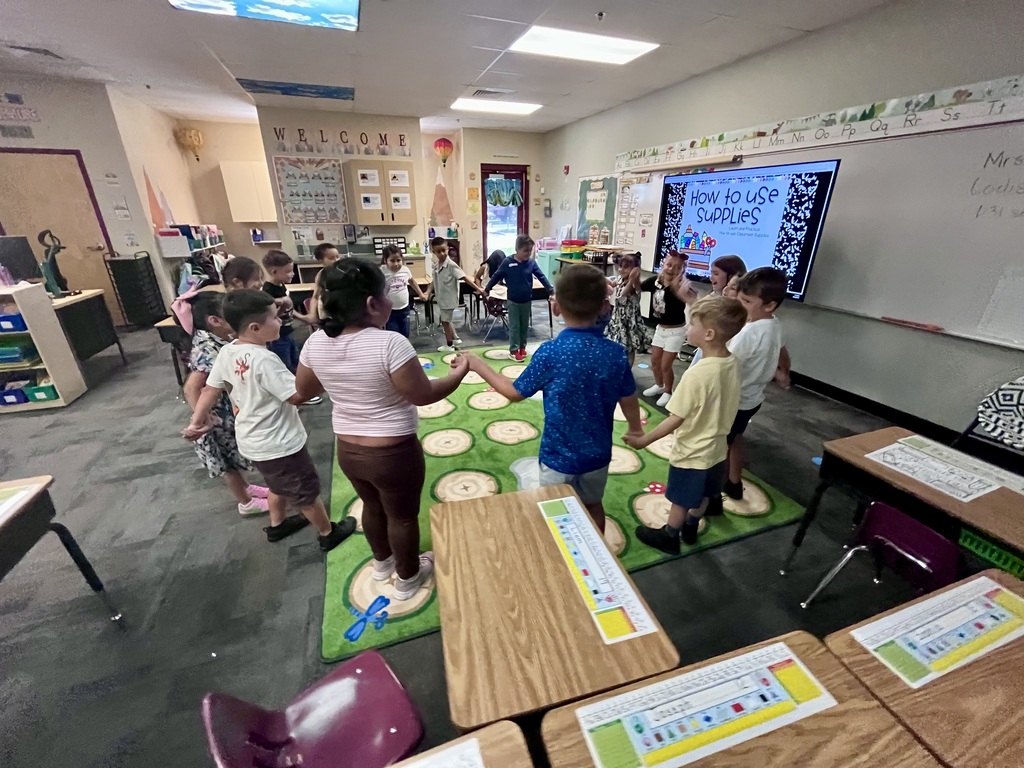 children in a circle standing in t a classroom