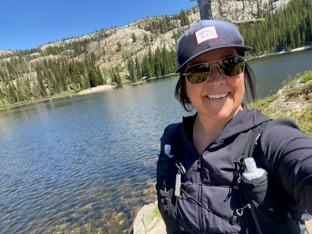 Cynthia Anderson on a hike by a beautiful lake and mountains.
