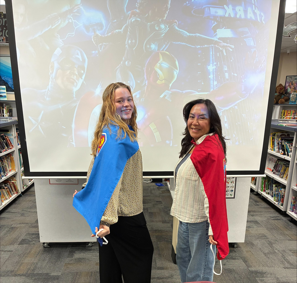 An image of 2 teachers in front of a superhero background