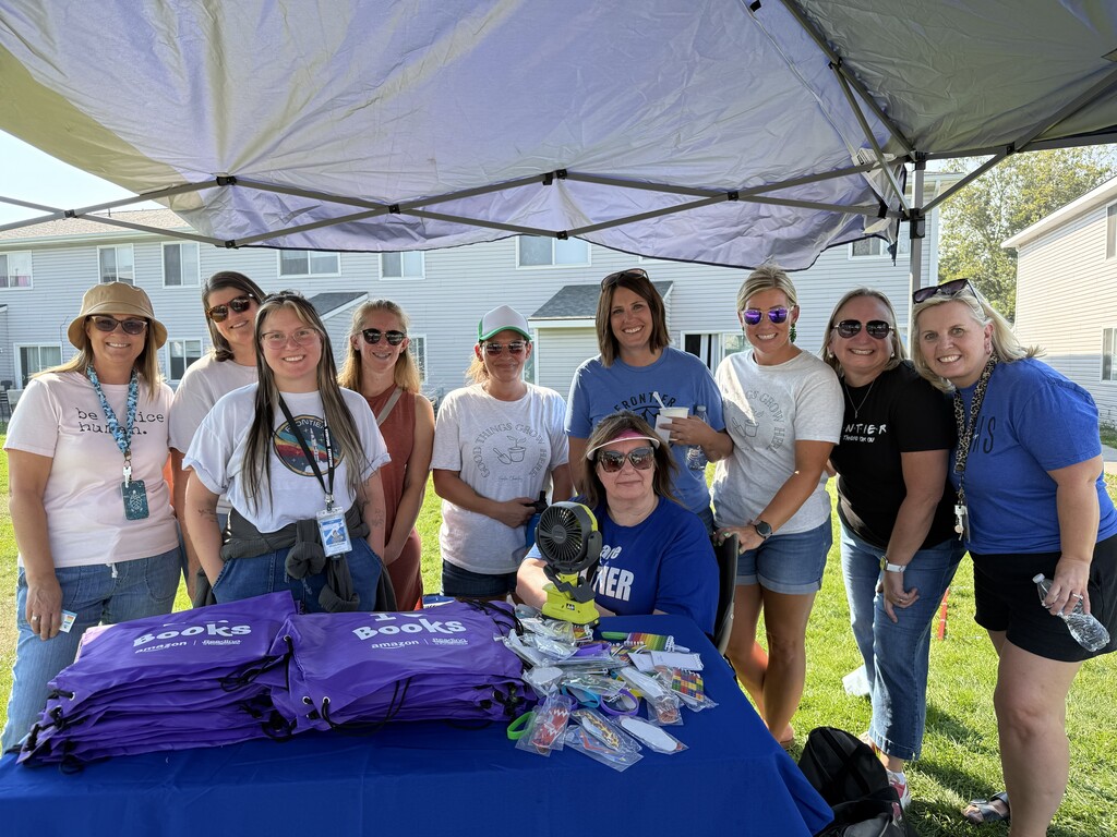 A photo of several Frontier staff members standing behind a table full of book bags at National Night Out at the Northwest Pointe Apartments.