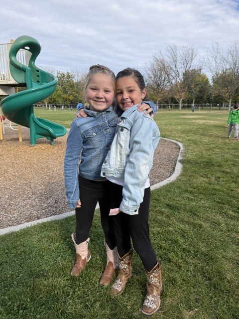 two girls wearing jean jackets, black pants, and cowboy boots