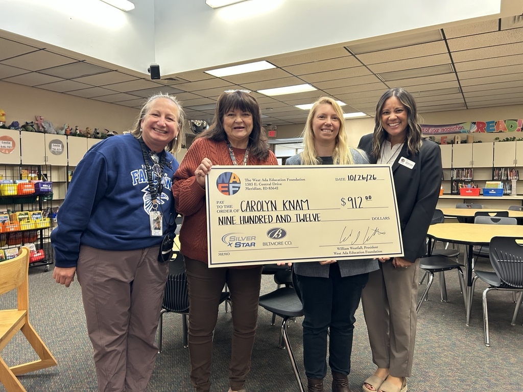 Four smiling women pose for a photo in the Frontier Elementary library. Mrs. Carolyn Knam holds a large ceremonial check for $912 from the West Ada Education Foundation, sponsored by Silver Star and Biltmore Co. The group celebrates the grant award, which will support the school library.