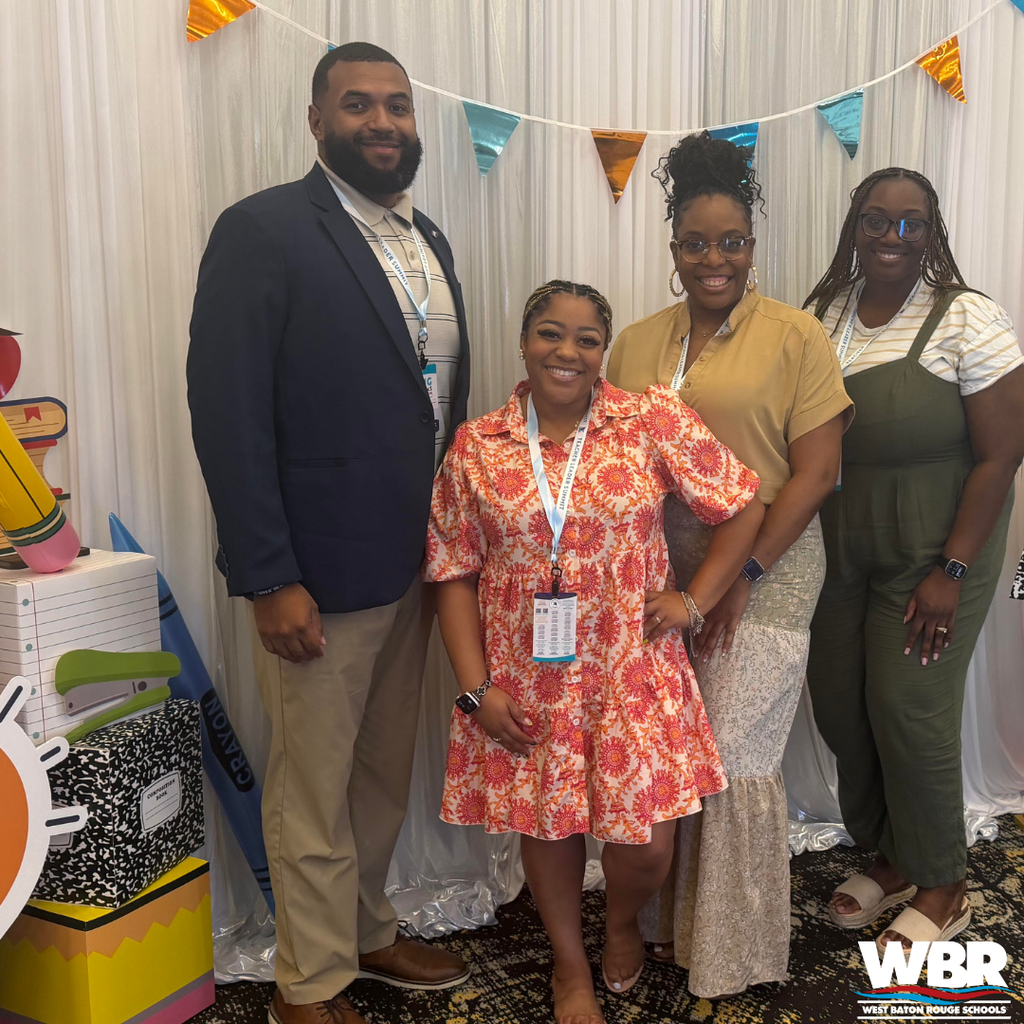 Four people stand together at an event, smiling for the camera. A colorful backdrop with bunting is behind them.
