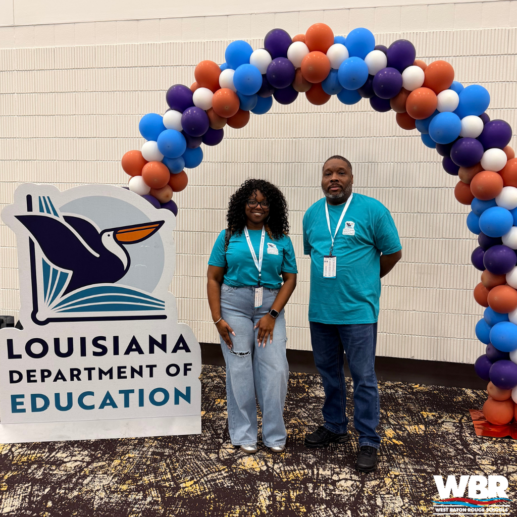 A man and woman stand under a balloon arch, smiling, in front of a Louisiana Department of Education sign.