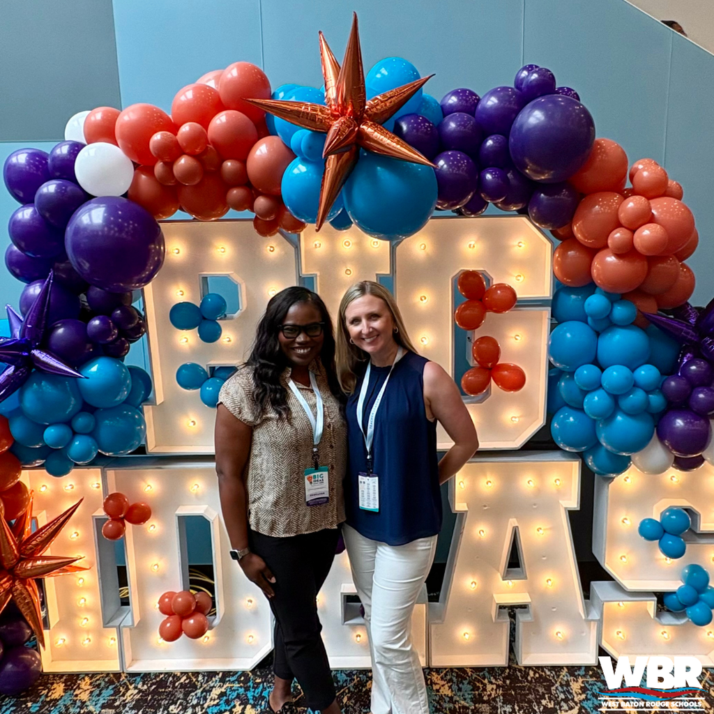 Two women pose in front of a colorful balloon arch and sign with "Big Ideas" displayed prominently.
