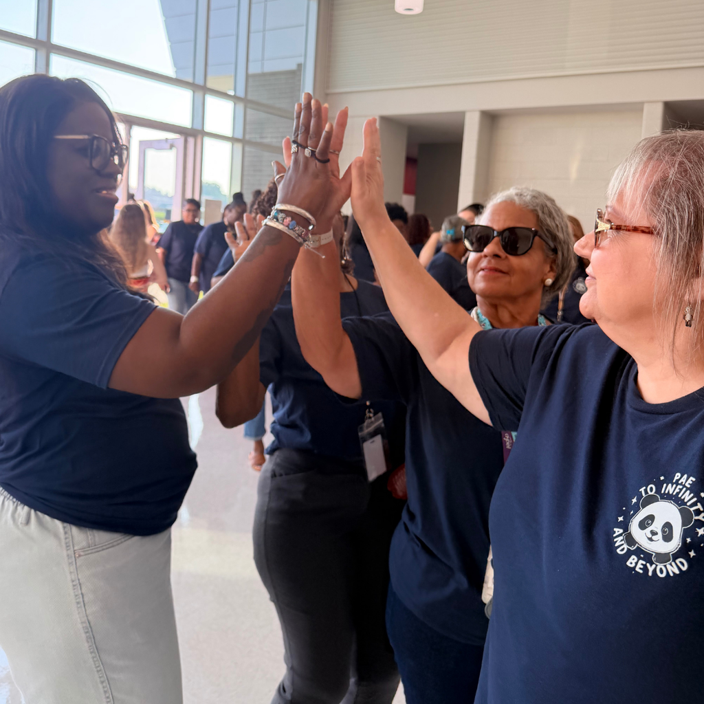 Two women in matching shirts with a panda logo giving high-fives, with others standing in a blurred background.