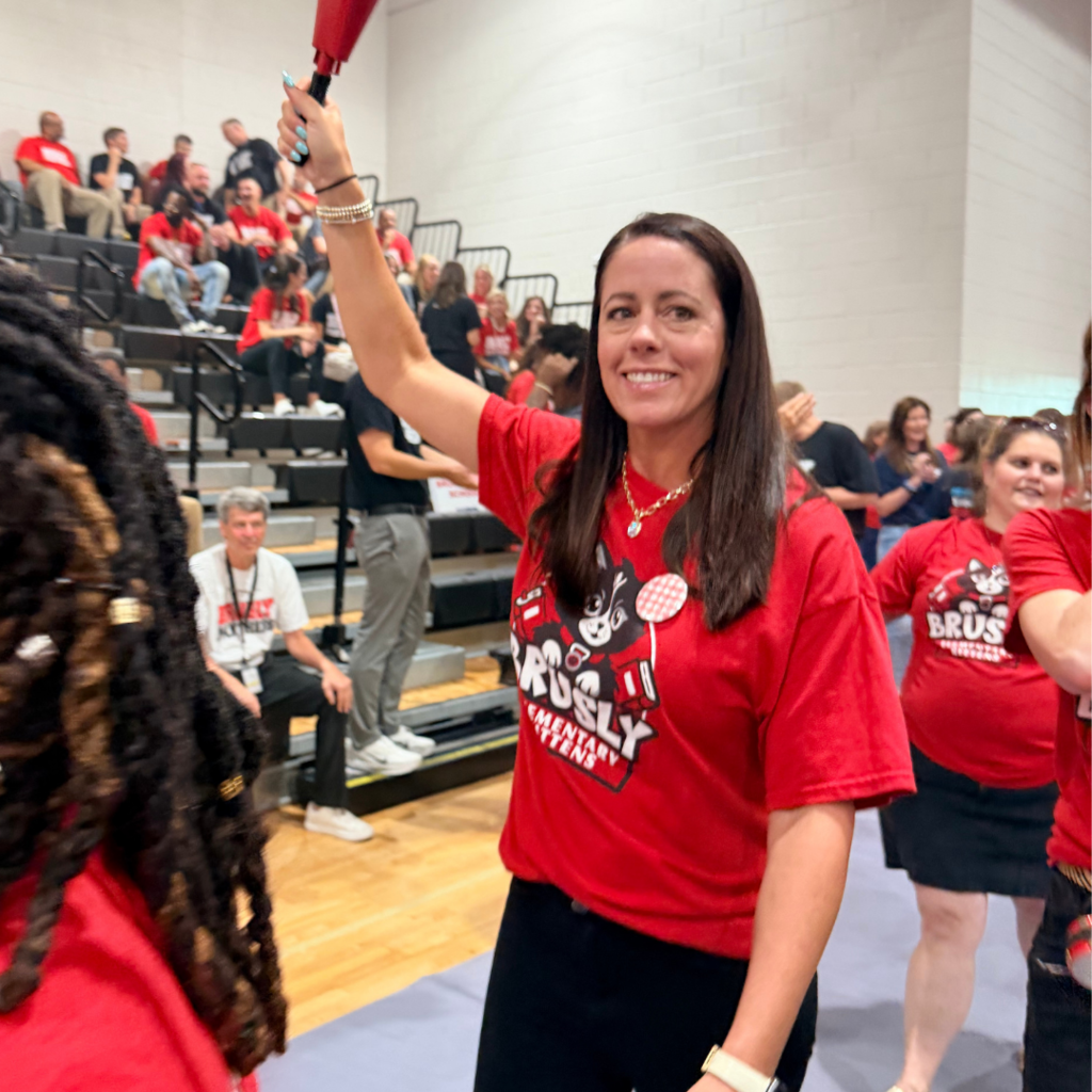 A woman waves a red object in a stadium. She and others wear red shirts with logos.