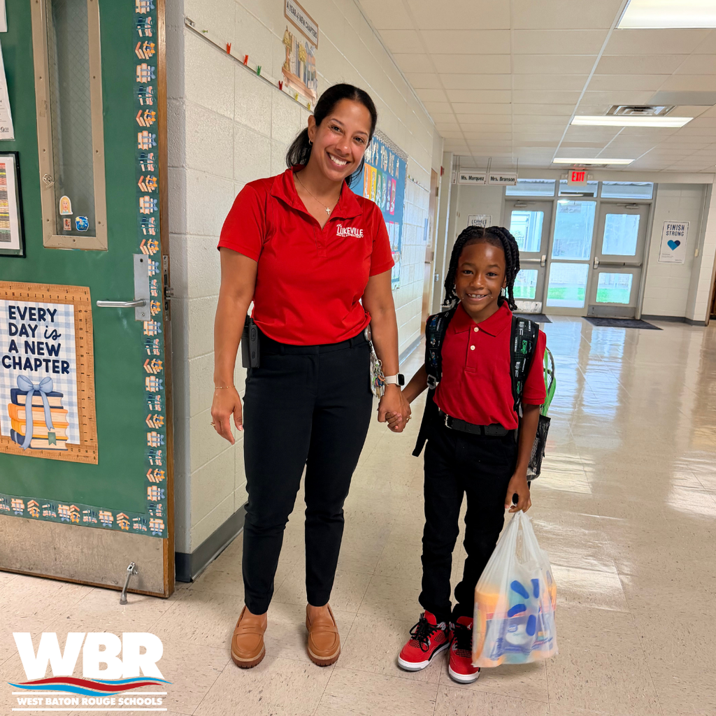 A woman and a child in matching red shirts stand in a school hallway, smiling. The woman holds the child's hand.