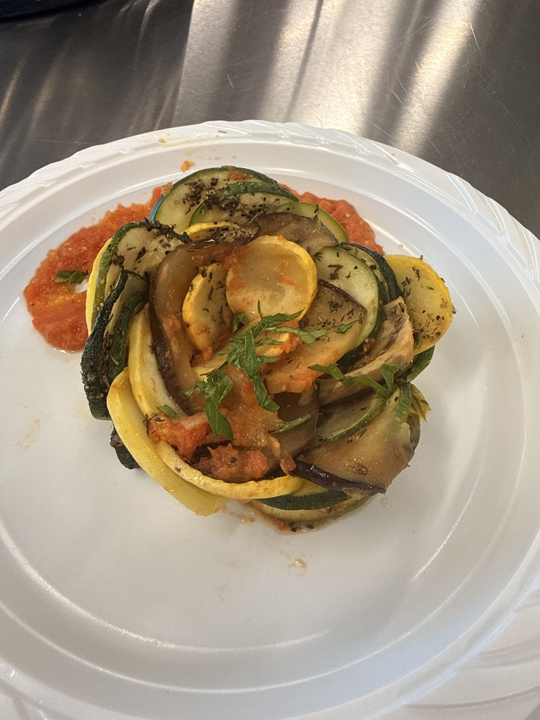 A white plate holds spiraled zucchini with red sauce on a metal surface. The plate is slightly tilted.