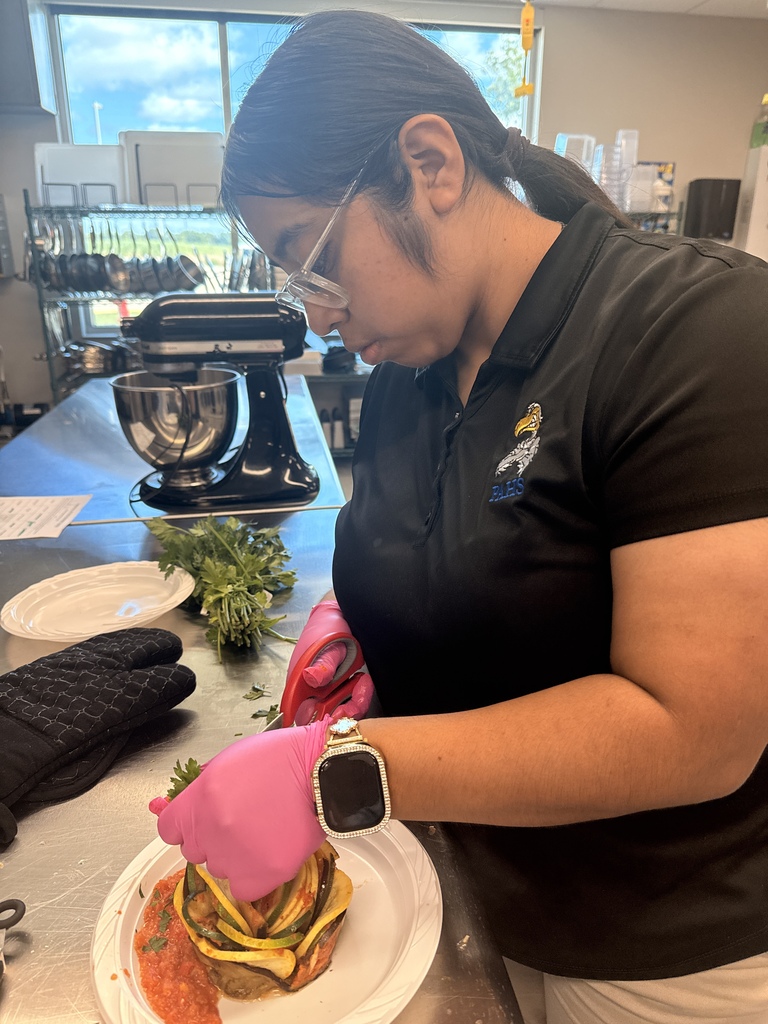 Person in black shirt and pink gloves working on food on a white plate in a kitchen.