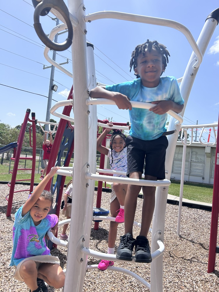 Two children climb a white metal structure. A girl in pink shoes and a boy in a blue shirt.