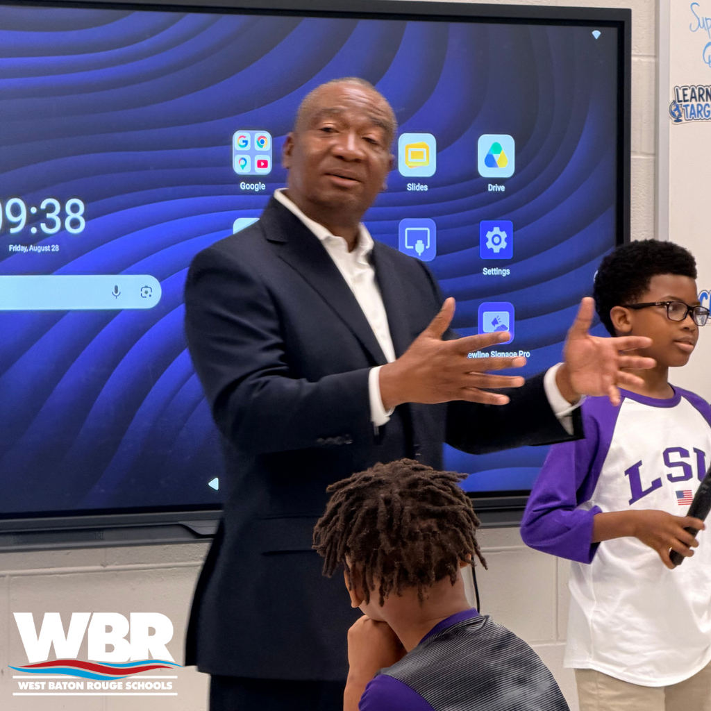 A man in a suit speaks in front of a screen and three students listen.