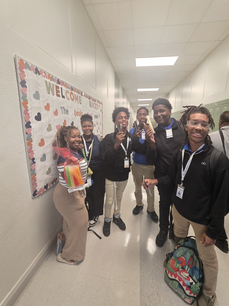 People in a hallway, posing with ID cards. A wall displays a banner with colorful hearts and text.