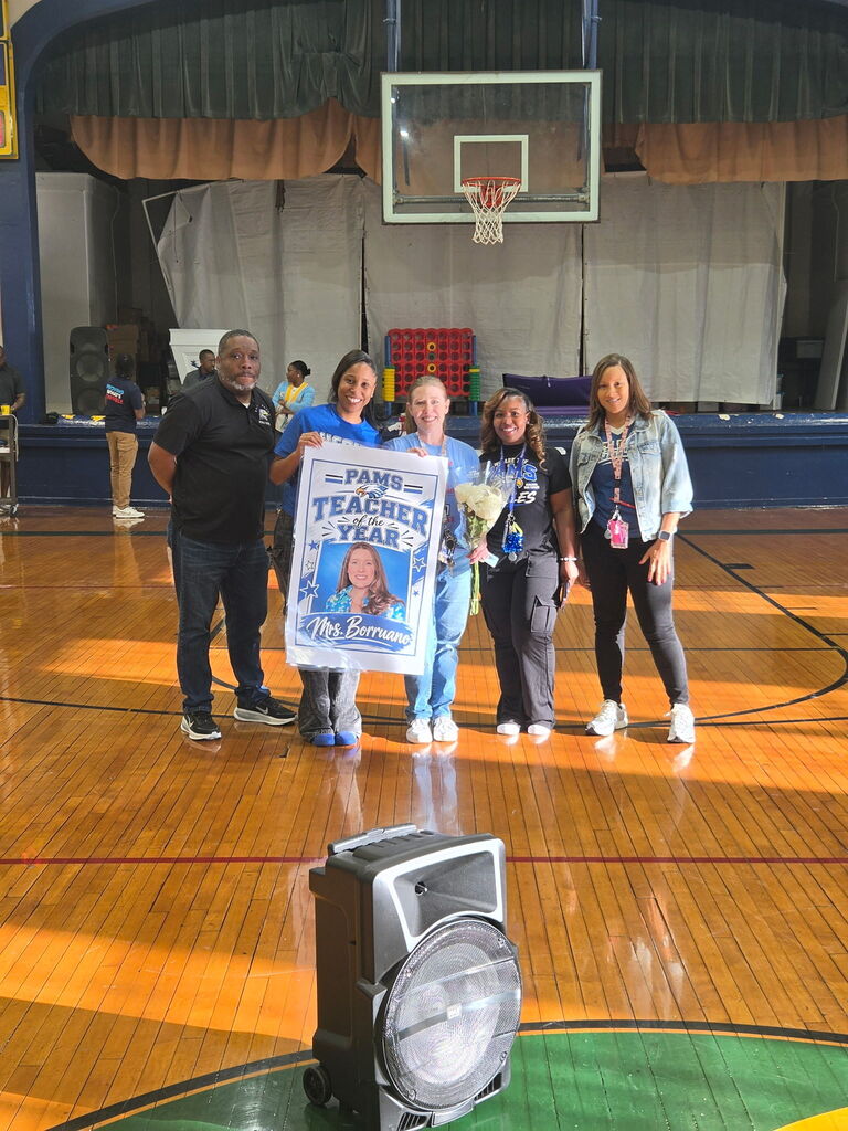 A group of adults and one child in a gym, standing next to a basketball hoop. The child holds a sign.