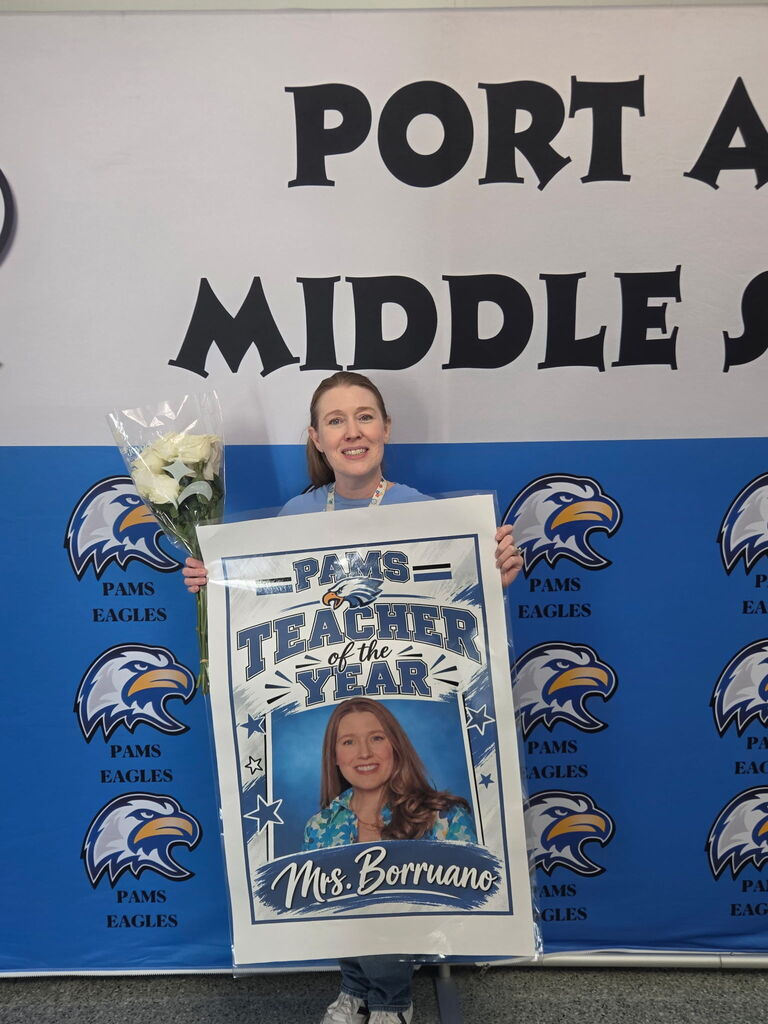 A person holds a sign that says "Teacher of the Year" with a picture of Ms. Borruano.