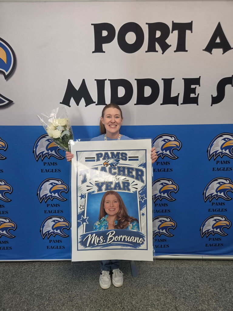 Person holding poster that says "PAMS TEACHER OF THE YEAR" with photo of a woman.